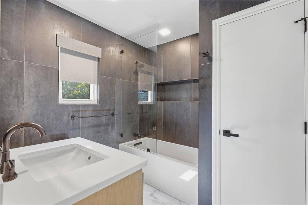 Modern bathroom featuring textured gray wall tiles, a white vanity with an integrated sink, and a bronze-finish faucet