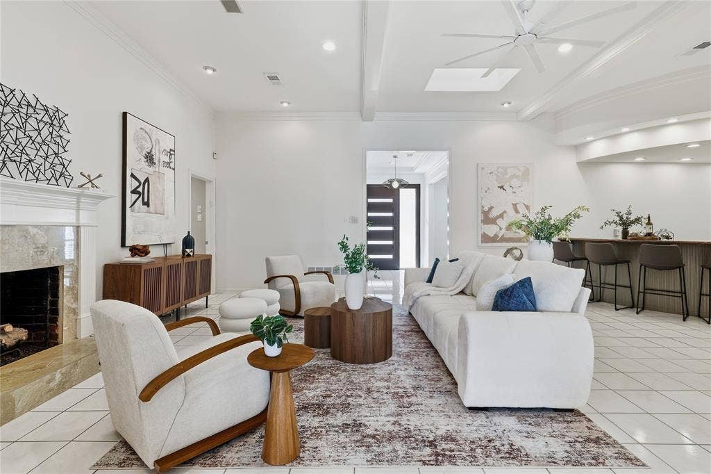 Spacious living area featuring a fireplace with a stone surround, tiled flooring, high ceilings with exposed beams, recessed lighting, and a built-in bar
