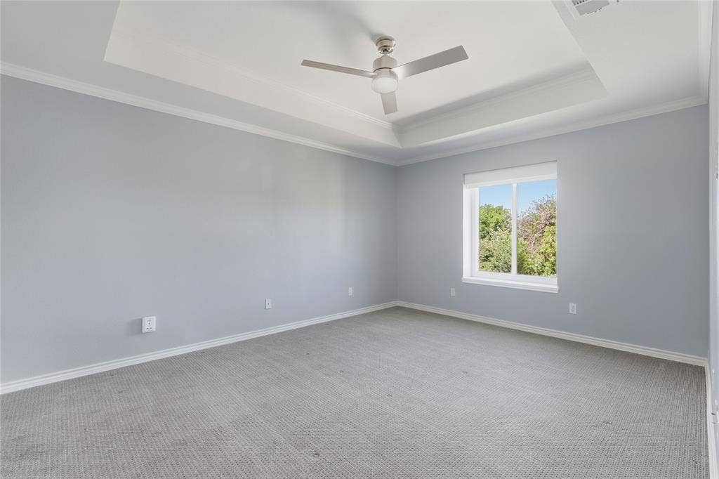 Tray ceiling with a ceiling fan, crown molding, double-pane window, and carpeted flooring