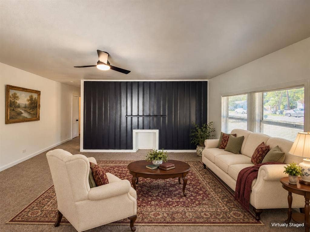 3709 N 22nd Street, Waco, TX 76708 Spacious living room featuring a ceiling fan with integrated lighting, black vertical blinds, large windows with natural light exposure, cream-upholstered seating, wood-finish side tables, and patterned area rug over carpeted flooring