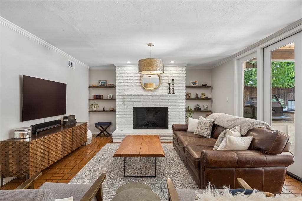 10428 Vinemont, Dallas, TX 75218 Whitewashed brick fireplace with a hearth, custom floating shelves, wood-finish flooring, and French doors leading to an exterior area