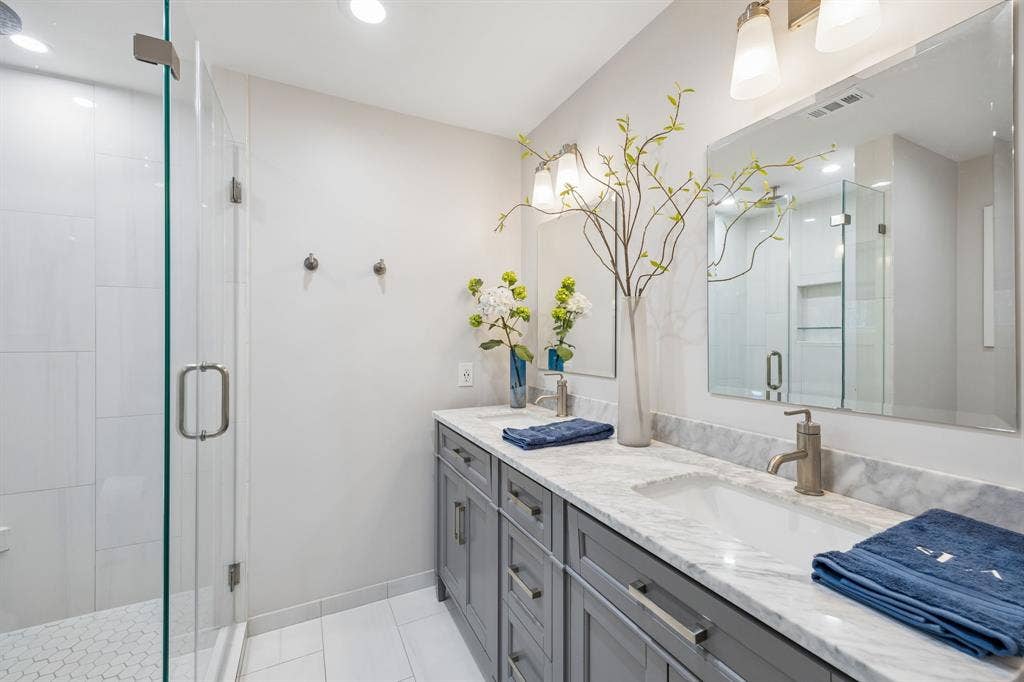 10428 Vinemont, Dallas, TX 75218 Double vanity with integrated sinks, brushed nickel fixtures, gray cabinetry with modern hardware, marble-look countertop, and a glass-enclosed shower