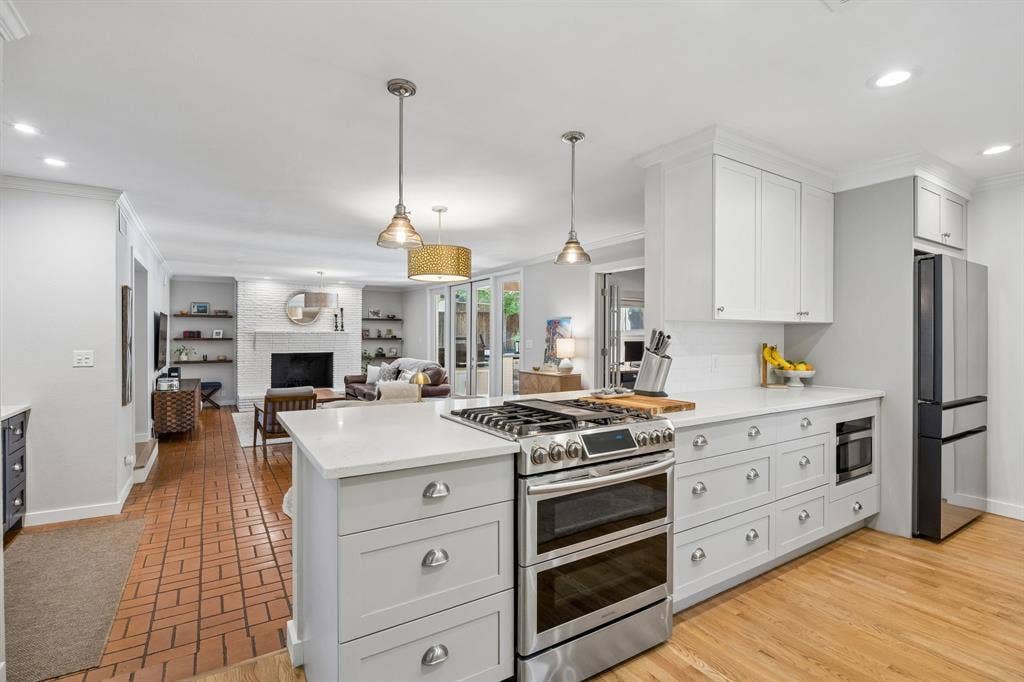 10428 Vinemont, Dallas, TX 75218 Stainless steel range with double ovens, white cabinetry, integrated microwave, wood-finish flooring, and brick-patterned flooring