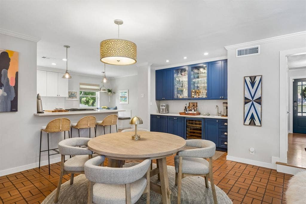 10428 Vinemont, Dallas, TX 75218 Dining area featuring terracotta tile flooring, a built-in wet bar with blue cabinetry and glass-front upper cabinets, and a kitchen pass-through with pendant lighting