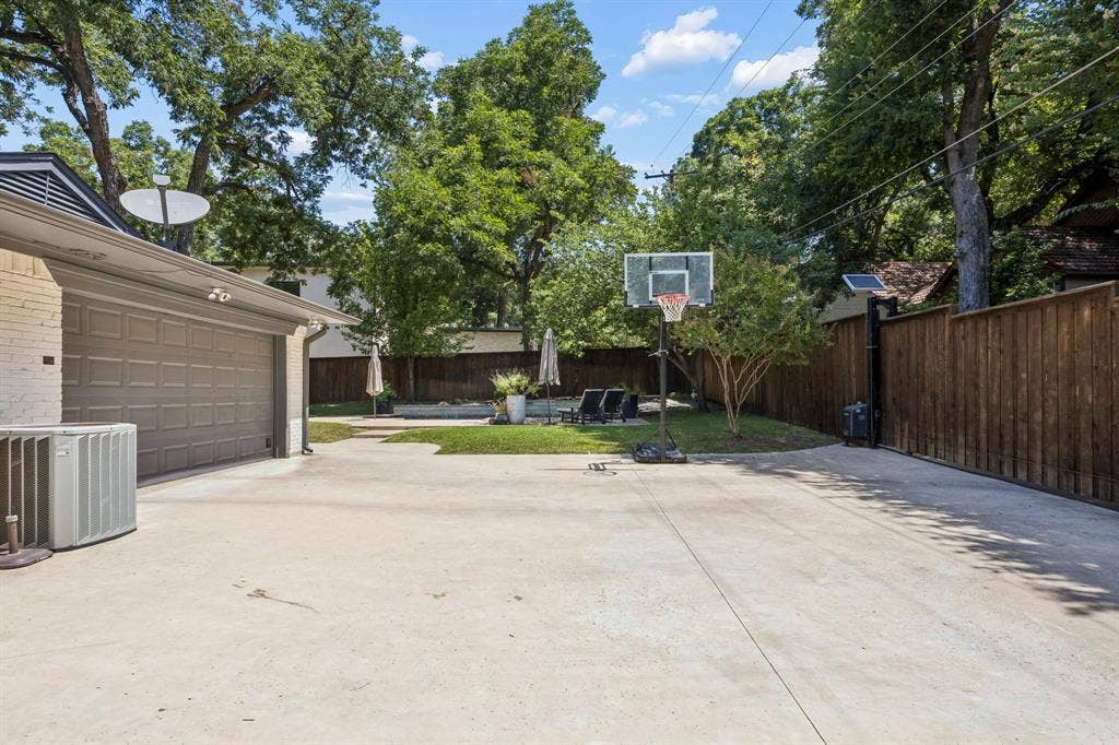 10428 Vinemont, Dallas, TX 75218 Spacious concrete driveway, attached two-car garage with a paneled door, privacy fence, and manicured lawn