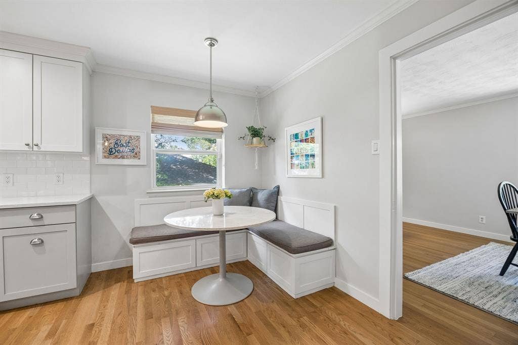 10428 Vinemont, Dallas, TX 75218 Light wood-finish flooring with white built-in banquette seating, white shaker-style cabinetry, white subway tile backsplash, and a polished chrome pendant light fixture