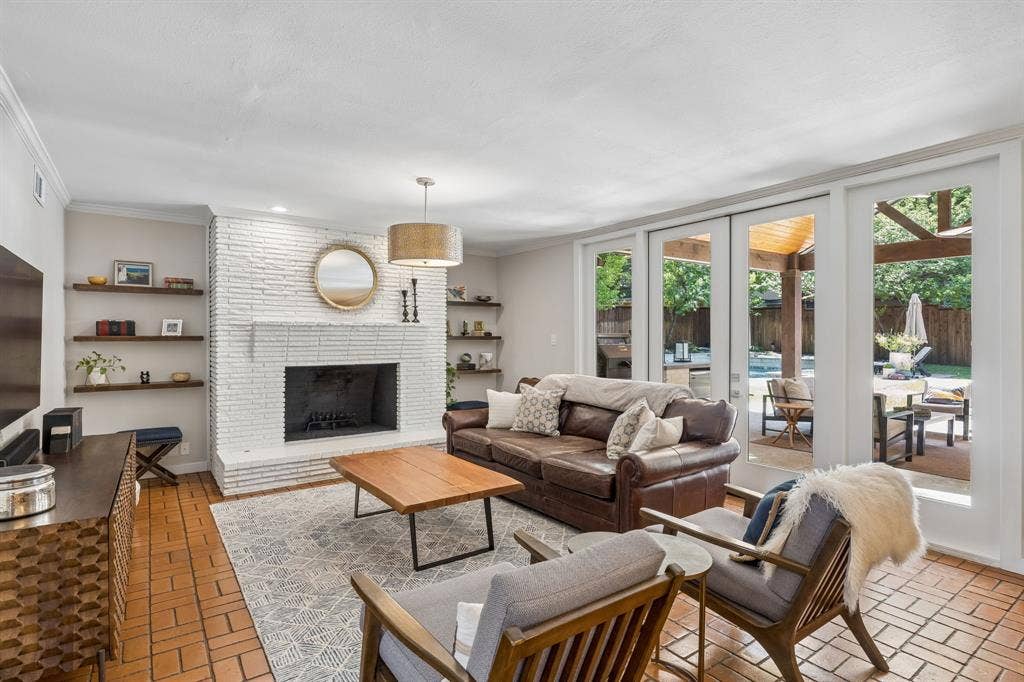 10428 Vinemont, Dallas, TX 75218 White brick fireplace with hearth, wood-finish floating shelves, terracotta tile flooring, and sliding glass panel doors