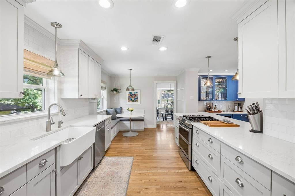 10428 Vinemont, Dallas, TX 75218 Open-concept kitchen featuring wood-finish flooring, white subway tile backsplash, white and gray cabinetry, and a built-in banquette with a round table