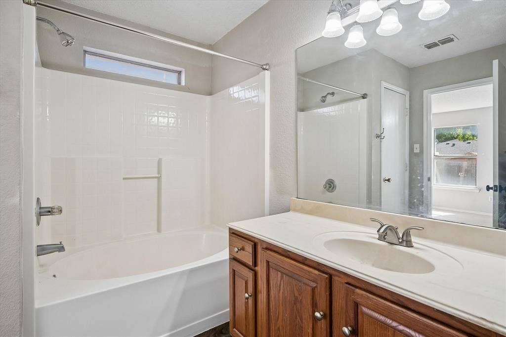 Built-in bathtub with shower, wood-finish vanity with countertop, and large wall mirror