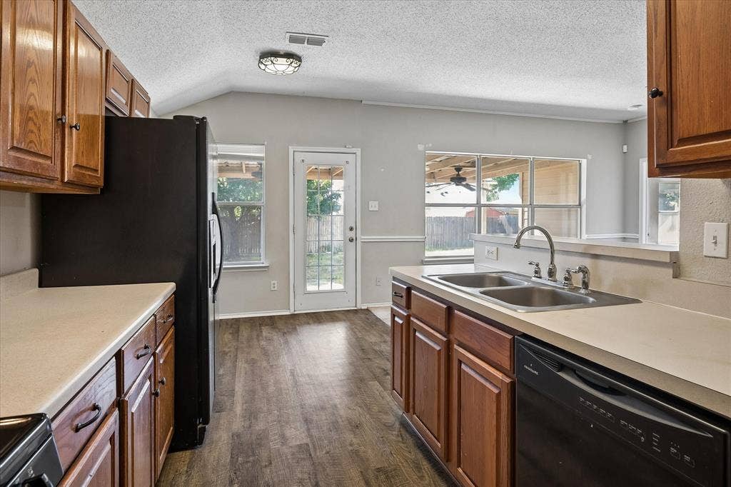 Kitchen featuring wood-finish flooring, ample wood cabinetry, a double basin sink, and a black dishwasher