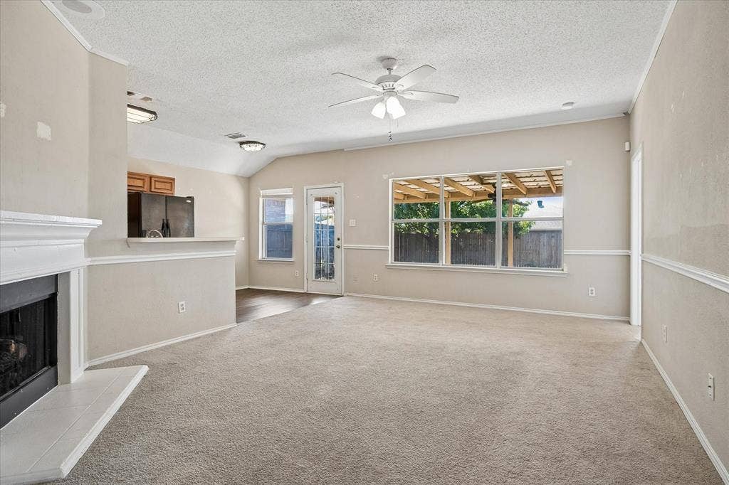 Spacious living area featuring a fireplace, vaulted ceiling, ceiling fan with integrated lighting, and direct outdoor access