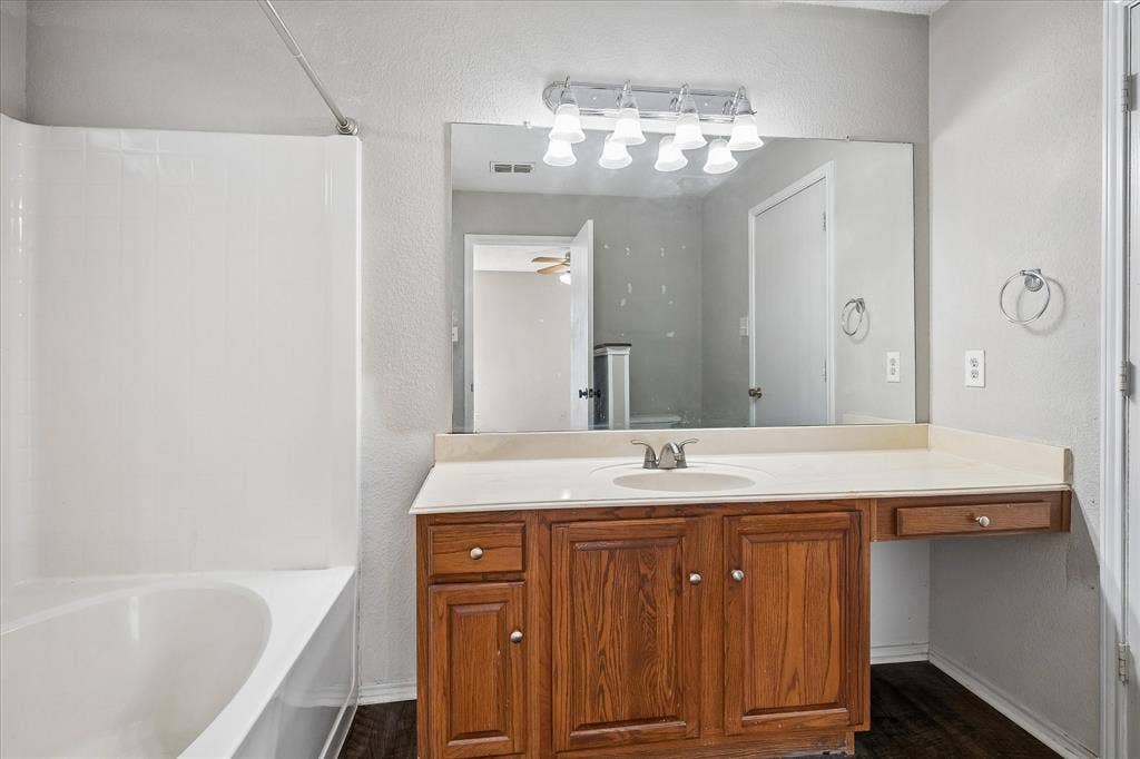 Bathroom featuring a wood-finish vanity with an integrated sink and light-toned countertop, a large wall-mounted mirror, and a white shower/tub combination