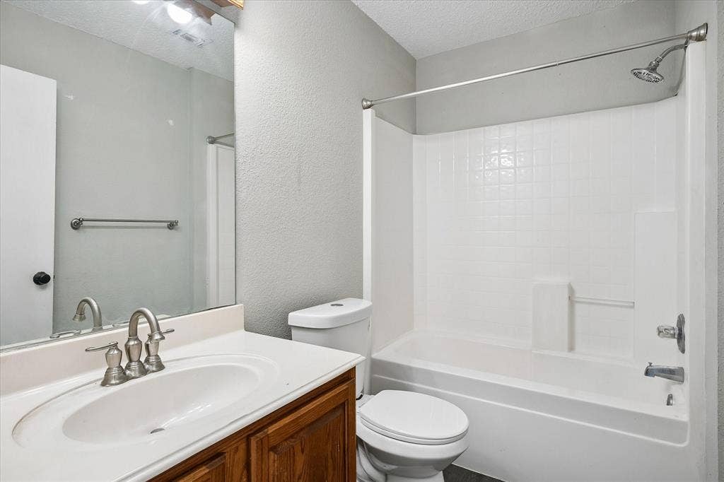 Bathroom featuring a vanity with an integrated sink, brushed nickel faucet, wood-finish cabinetry, and a shower-over-tub combination with white tile-patterned surround
