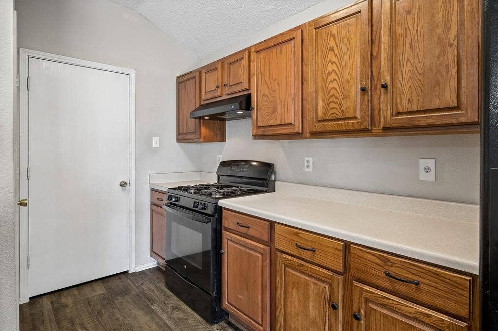 Kitchen featuring wood-finish cabinetry, solid surface countertops, a black gas range, and wood-finish flooring
