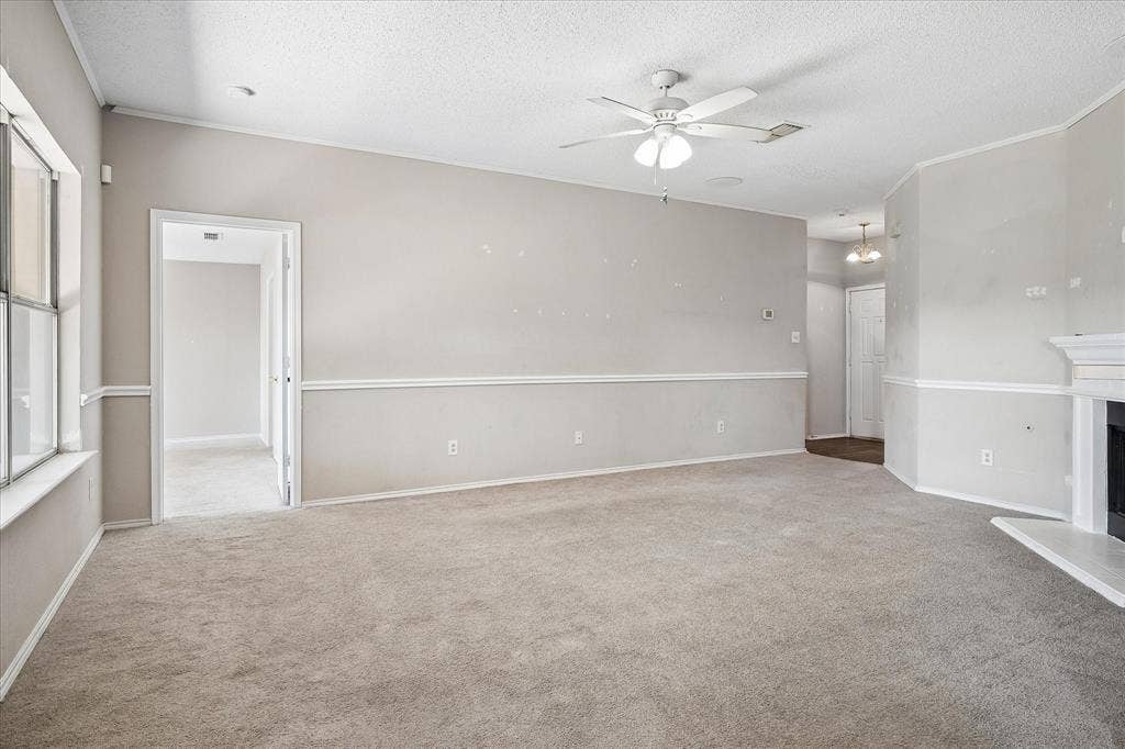 Carpeted room with a ceiling fan, crown molding, and a fireplace