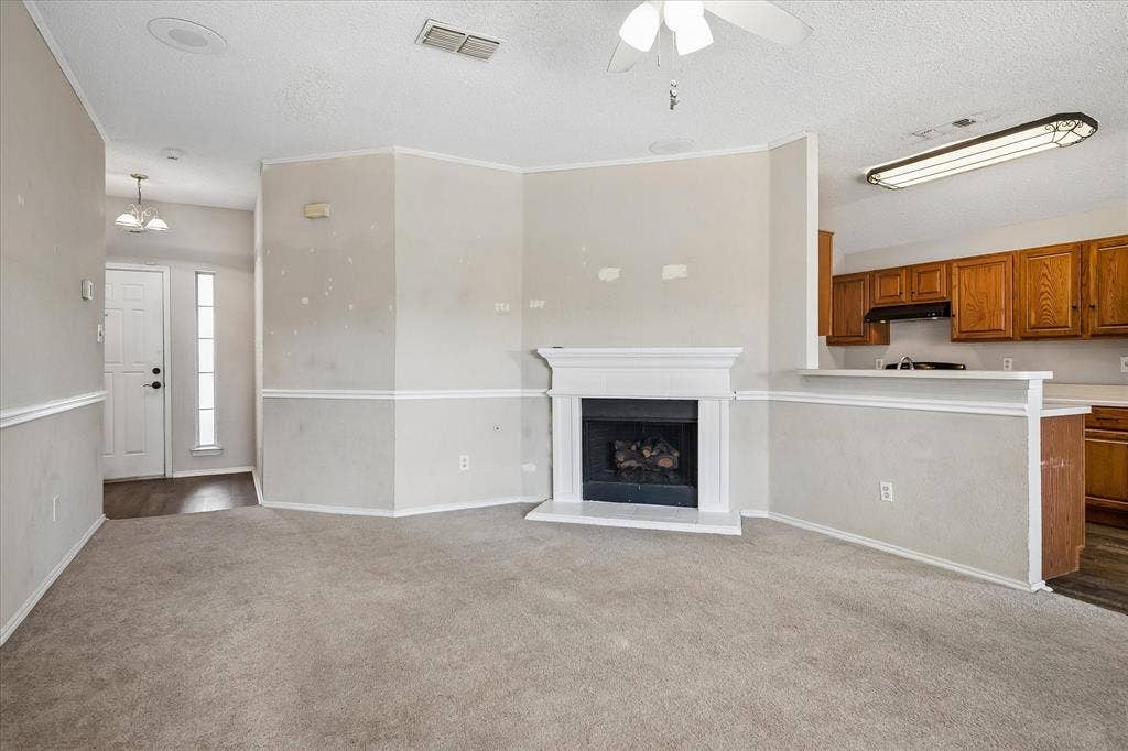 Carpeted living area with a fireplace and mantel, crown molding, and a ceiling fan