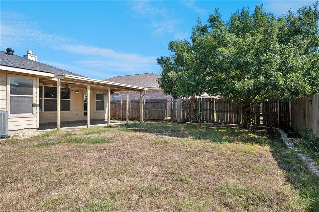 Expansive backyard featuring a covered patio, mature tree, and wood privacy fencing