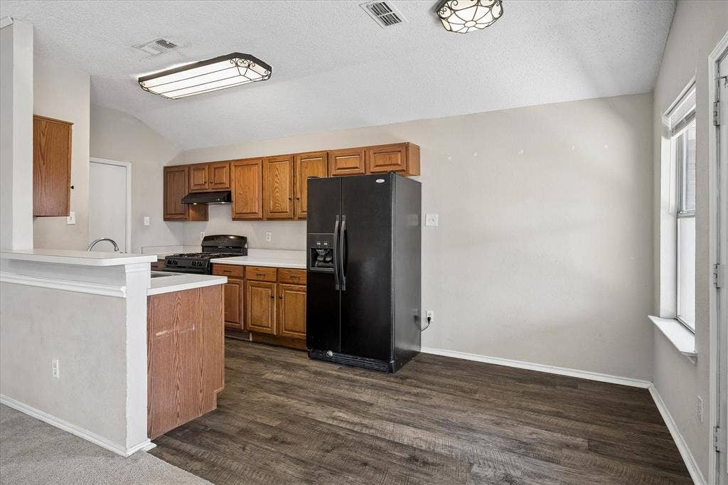 Kitchen area featuring wood-finish flooring, wood cabinetry, built-in black appliances, and a window for natural light