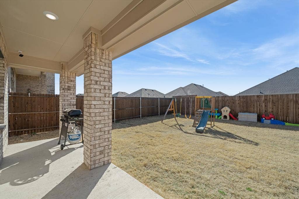 202 Buckboard Lane, Caddo Mills, TX 75135 A shaded concrete back patio supported by handsome brick masonry columns offers an inviting outdoor retreat at 202 Buckboard Ln. The expansive, flat backyard is fully secured by full-height wood privacy fencing with durable metal posts, creating a private outdoor living space ideal for pets, recreation, and open-air entertaining. Recessed lighting under the covered porch accommodates evening gatherings, while the level lawn provides plenty of room for play structures or future landscape design beneath open Texas skies in Caddo Mills.