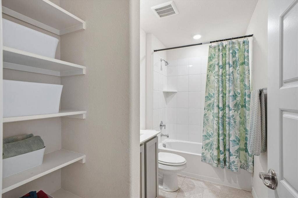 202 Buckboard Lane, Caddo Mills, TX 75135 Inside 202 Buckboard Ln in Caddo Mills, this well-appointed full bathroom showcases practical organization and neutral finishes. A deep built-in linen alcove features tiered floating shelves for convenient towel and toiletry storage. Clean ceramic tile flooring extends across the room toward the single-sink vanity, commode, and full bathtub-shower combination lined with classic white ceramic wall tile and chrome fixtures. Recessed ceiling lighting completes this bright, functional bath space designed for effortless daily living.