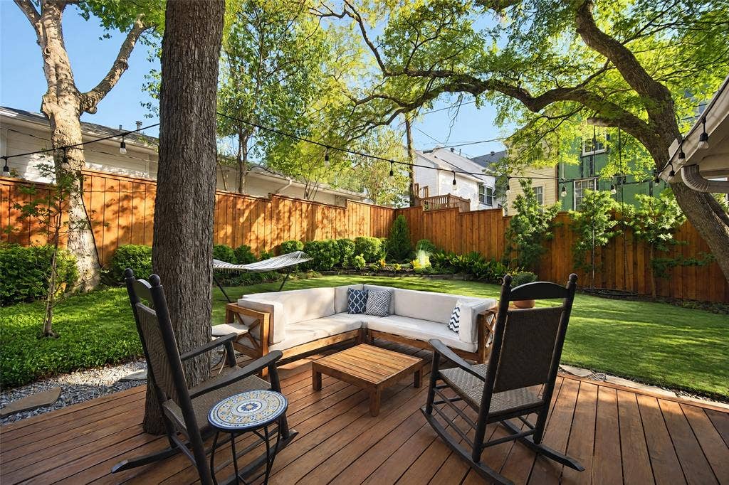 6866 Burwood Lane, Dallas, TX 75214 Expansive backyard with a wood deck, string lighting, mature trees, manicured lawn, and wood privacy fencing