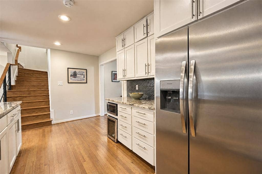 6866 Burwood Lane, Dallas, TX 75214 Stainless steel refrigerator, white cabinetry, granite countertops, tile backsplash, and wood flooring