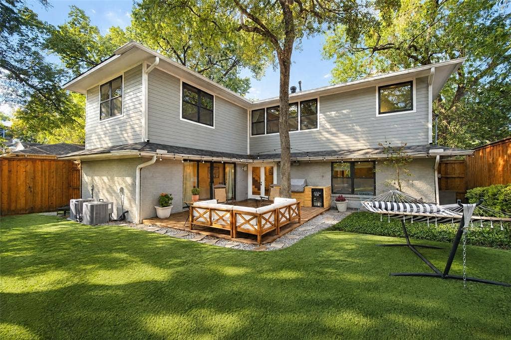 6866 Burwood Lane, Dallas, TX 75214 Expansive green lawn with a wood-plank deck, mature trees, and a privacy fence