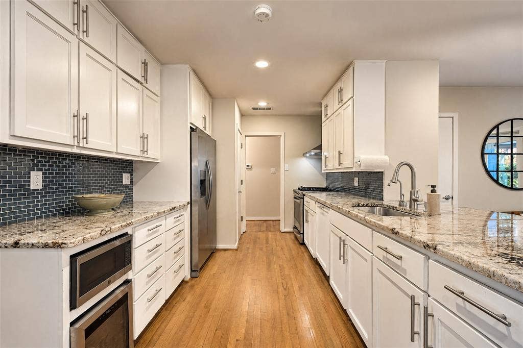 6866 Burwood Lane, Dallas, TX 75214 White shaker cabinetry, granite countertops, subway tile backsplash, stainless steel appliances, and wood-finish flooring