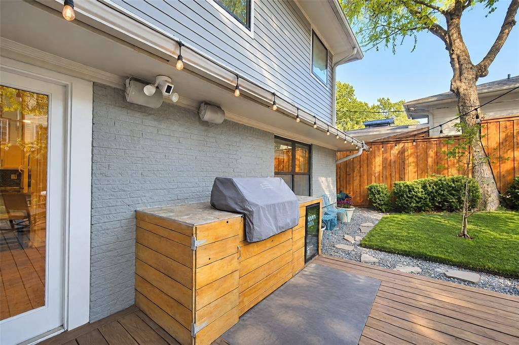 6866 Burwood Lane, Dallas, TX 75214 Expansive outdoor living area featuring a wood-finish deck, built-in outdoor kitchen, string lighting, and a manicured lawn area with stone pathway