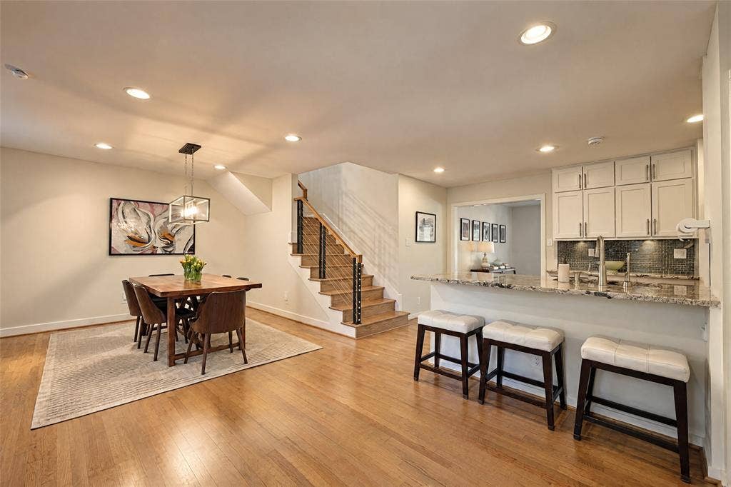 6866 Burwood Lane, Dallas, TX 75214 Hardwood flooring throughout, recessed lighting, modern stair railing with wood treads, kitchen island with stone countertop, and white kitchen cabinetry with backsplash
