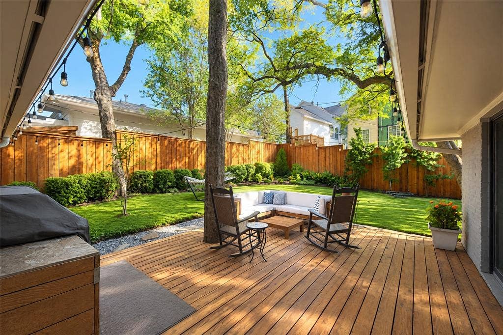 6866 Burwood Lane, Dallas, TX 75214 Expansive wooden deck, string lighting, manicured lawn, full privacy fencing, and mature trees