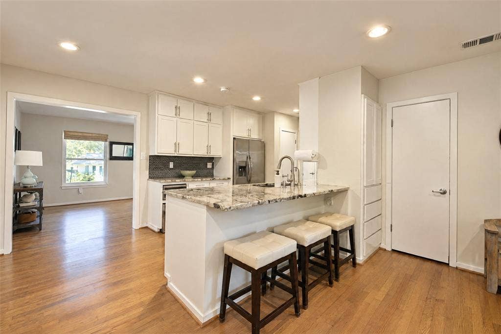 6866 Burwood Lane, Dallas, TX 75214 Kitchen featuring a granite-finish island with seating, stainless steel appliances, white cabinetry, and recessed lighting