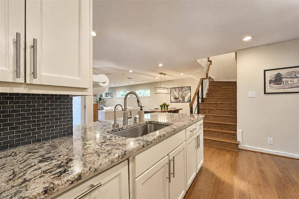 6866 Burwood Lane, Dallas, TX 75214 Kitchen island featuring a stainless steel sink, pull-down faucet, and light-toned stone countertops with dark veining