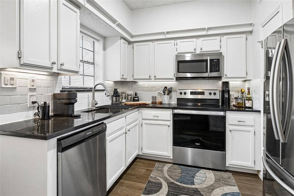 Kitchen featuring white shaker-style cabinetry, dark stone countertops, stainless steel appliances, and a subway tile backsplash