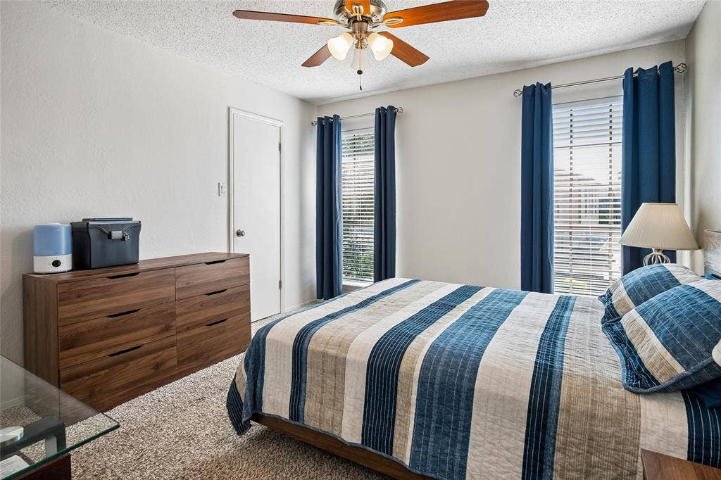 Bedroom featuring neutral wall paint, two dual-pane windows with horizontal blinds, textured ceiling, and a central ceiling fan with integrated lighting