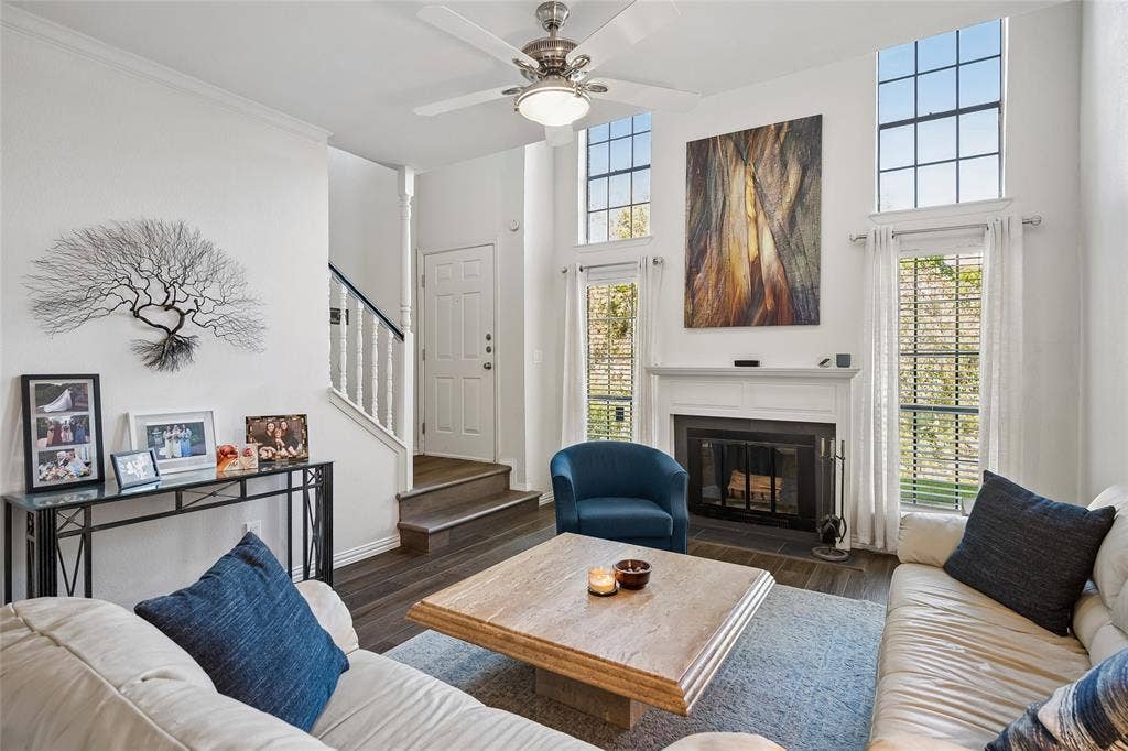 Living area featuring a double-height ceiling, fireplace with a mantel, tall paneled windows, wood-finish flooring, and a ceiling fan