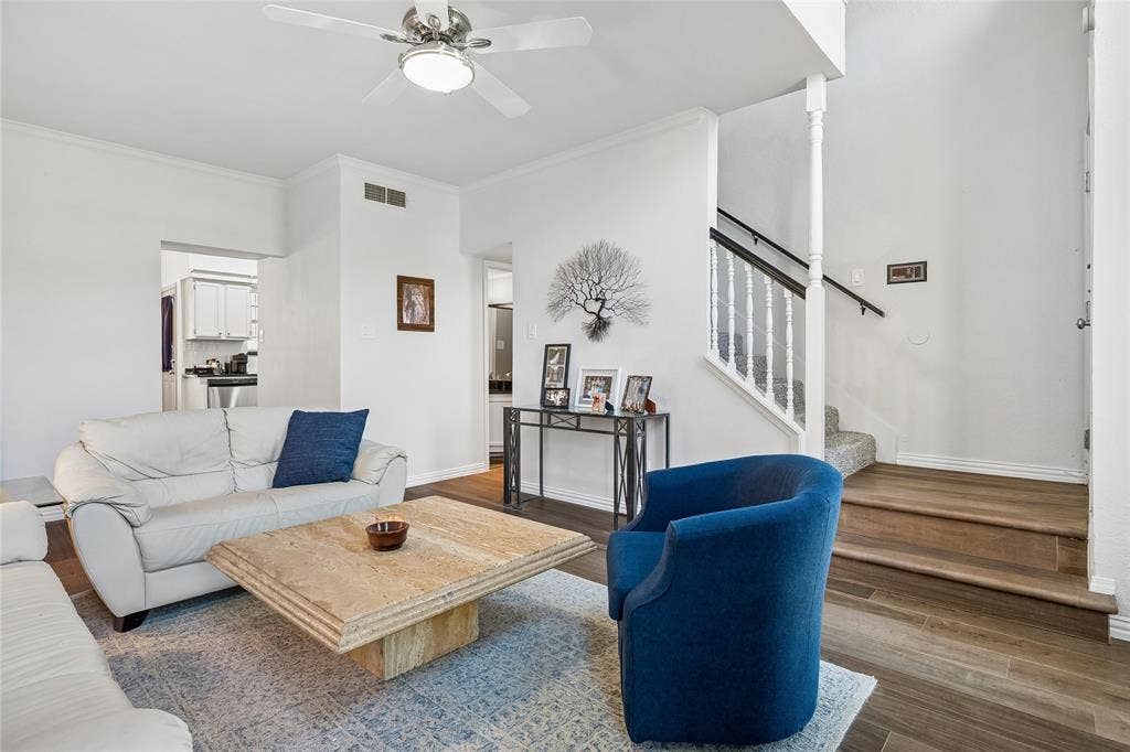 Living area featuring wood-finish flooring, staircase with a white balustrade and wooden handrail, and a ceiling fan with integrated lighting