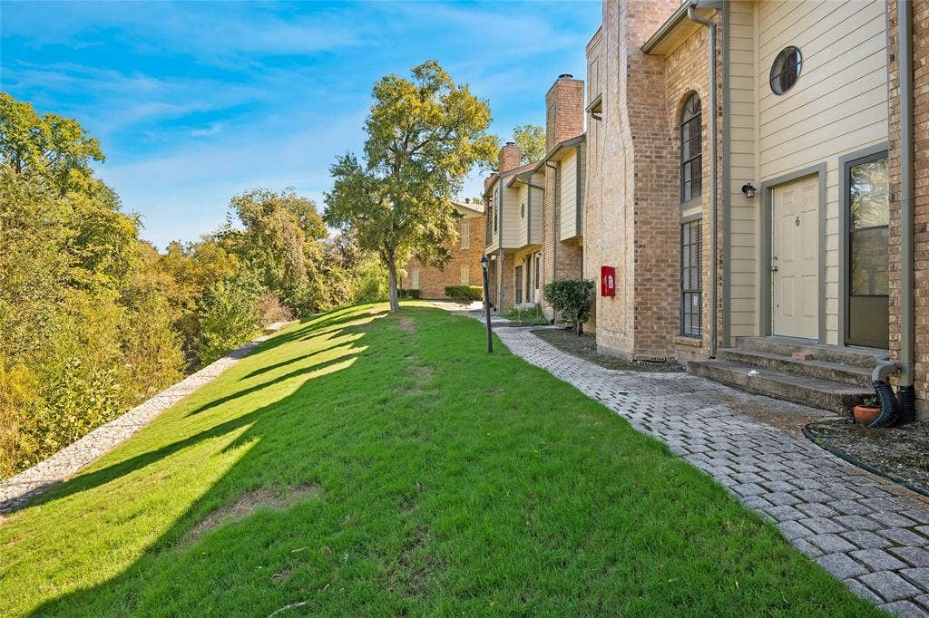Multi-level exterior featuring brick and siding construction, arched window accents, a paved stone walkway, and an expansive grass lawn with mature trees