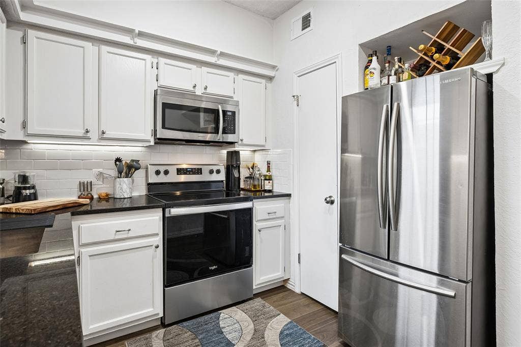 Kitchen featuring white shaker-style cabinetry, dark stone countertops, a white subway tile backsplash, and stainless steel appliances