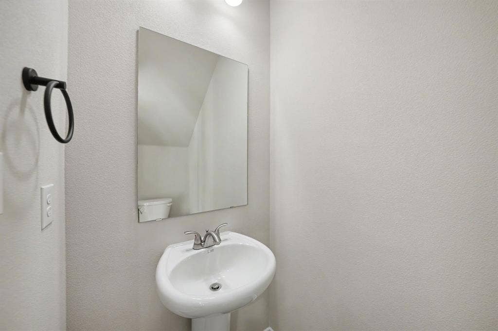 Pedestal sink with a chrome faucet, wall-mounted mirror, and a matte black towel ring