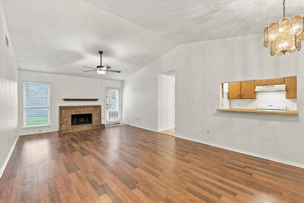 844 Woodrock Drive, Dallas, TX 75217 Vaulted ceiling with wood-finish flooring, brick fireplace with mantel, and a built-in kitchen pass-through