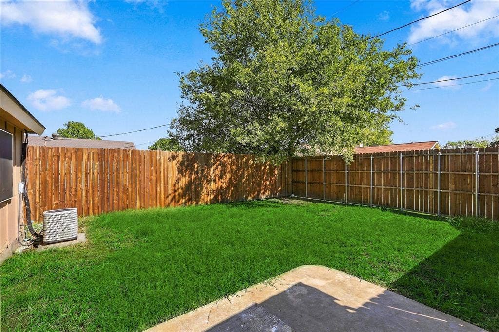 844 Woodrock Drive, Dallas, TX 75217 Expansive backyard featuring a manicured lawn, full privacy fencing, and mature tree