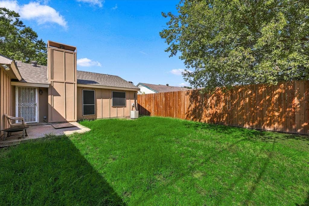 844 Woodrock Drive, Dallas, TX 75217 Expansive backyard featuring a manicured lawn, a full wood privacy fence, and a concrete patio