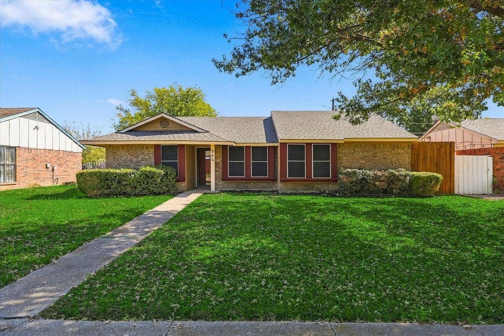 844 Woodrock Drive, Dallas, TX 75217 Brick facade, gabled entry, red window shutters, concrete walkway, and a wooden fence