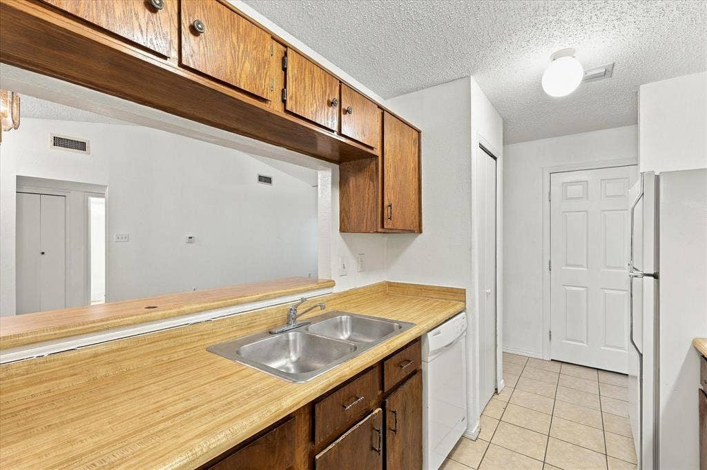 844 Woodrock Drive, Dallas, TX 75217 Kitchen featuring wood cabinetry, a pass-through window, a double basin stainless steel sink, tiled flooring, and a white refrigerator