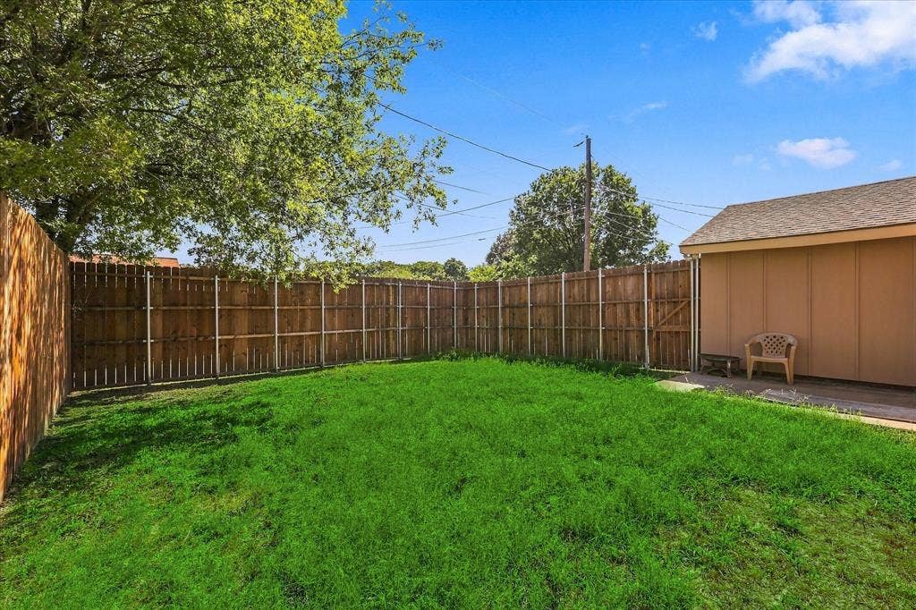 844 Woodrock Drive, Dallas, TX 75217 Expansive grassy area with wood fencing and a storage structure