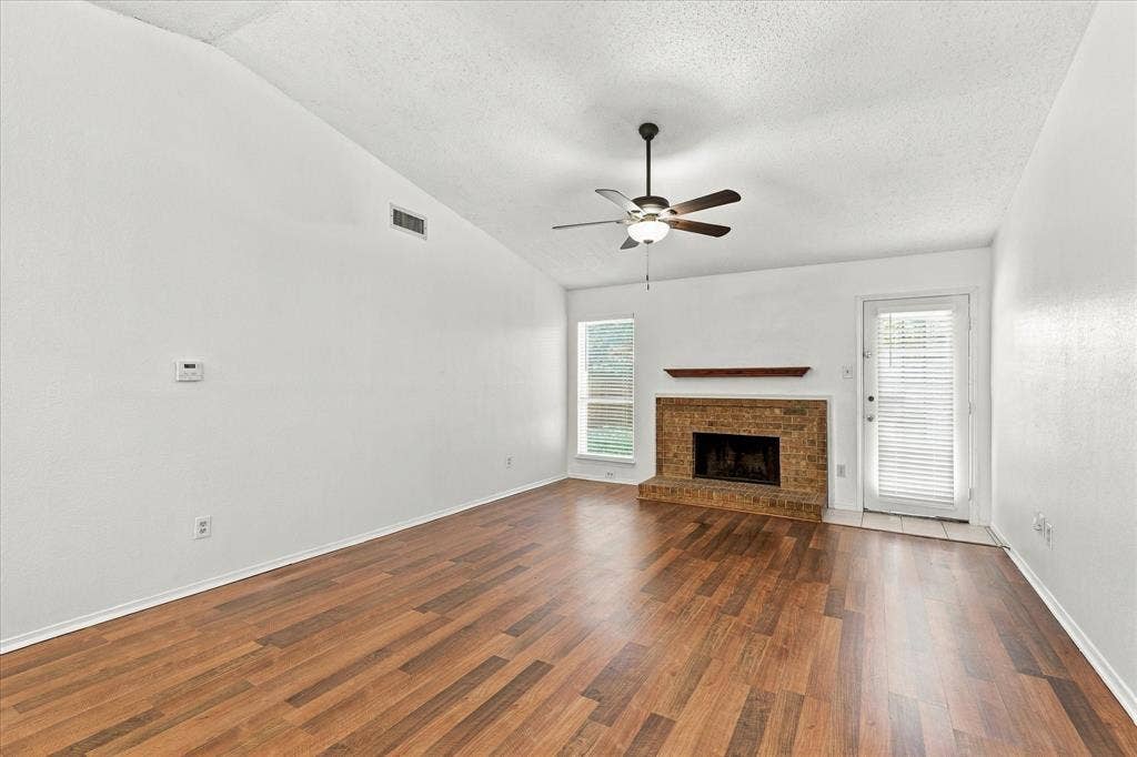 844 Woodrock Drive, Dallas, TX 75217 Vaulted ceiling with a ceiling fan, brick fireplace with a wood mantel, wood-finish flooring, and multiple windows