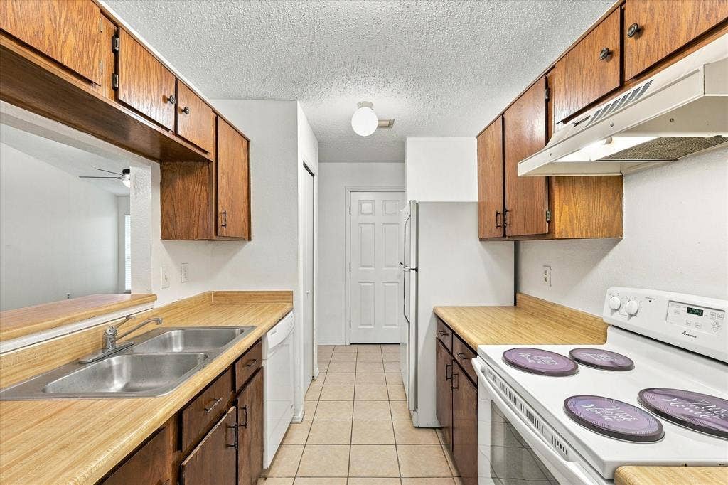 844 Woodrock Drive, Dallas, TX 75217 Galley kitchen featuring wood-finish countertops, wood cabinetry, and a double basin stainless steel sink