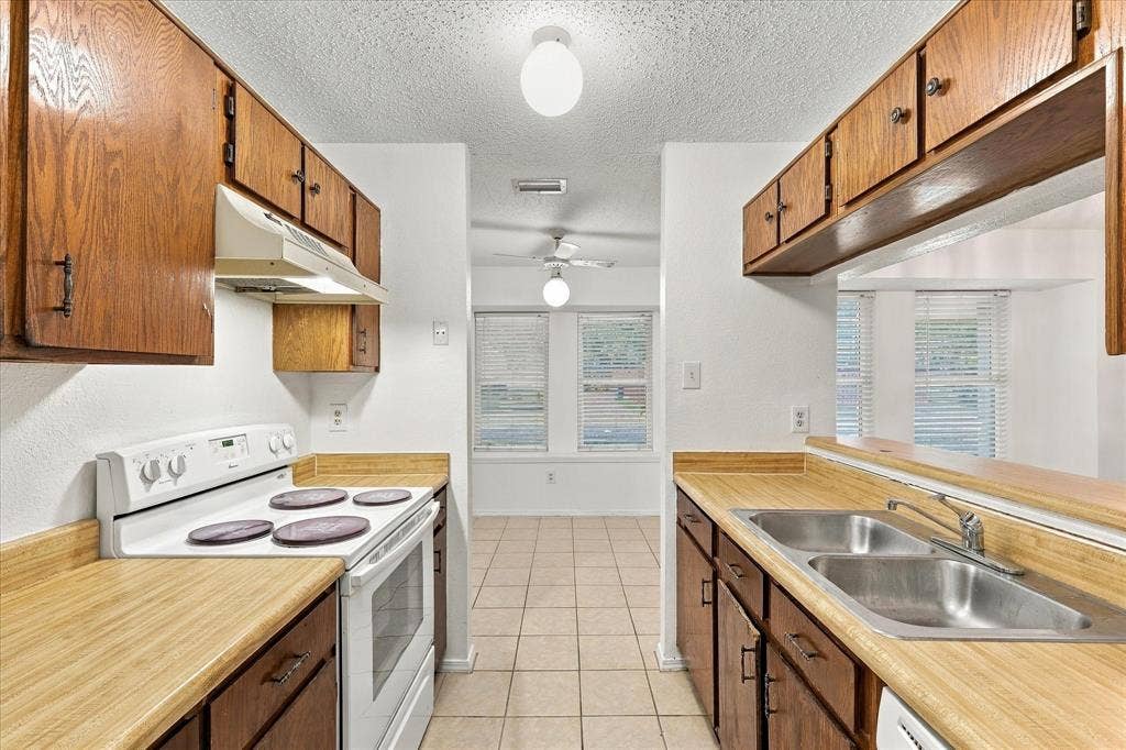 844 Woodrock Drive, Dallas, TX 75217 Galley kitchen featuring wood-finish cabinetry, a double basin stainless steel sink, a built-in range, and tile flooring