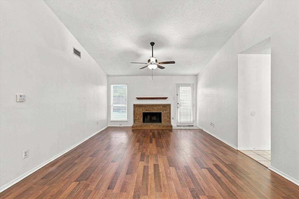 844 Woodrock Drive, Dallas, TX 75217 Vaulted ceiling, wood-finish flooring, brick fireplace with wood mantel, ceiling fan, and large window
